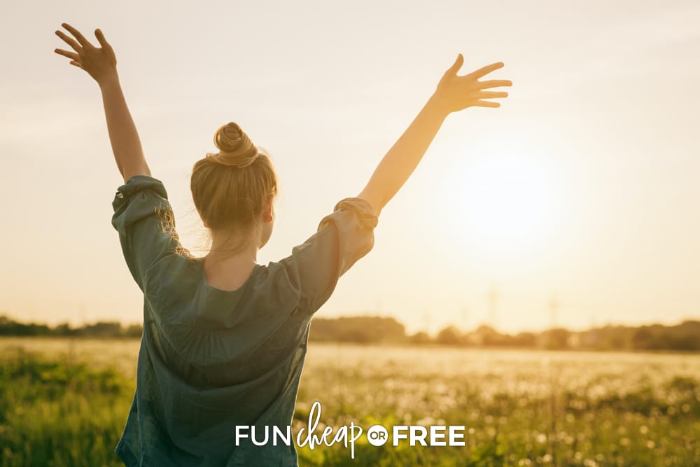 Woman throwing her hands up in a field, from Fun Cheap or Free