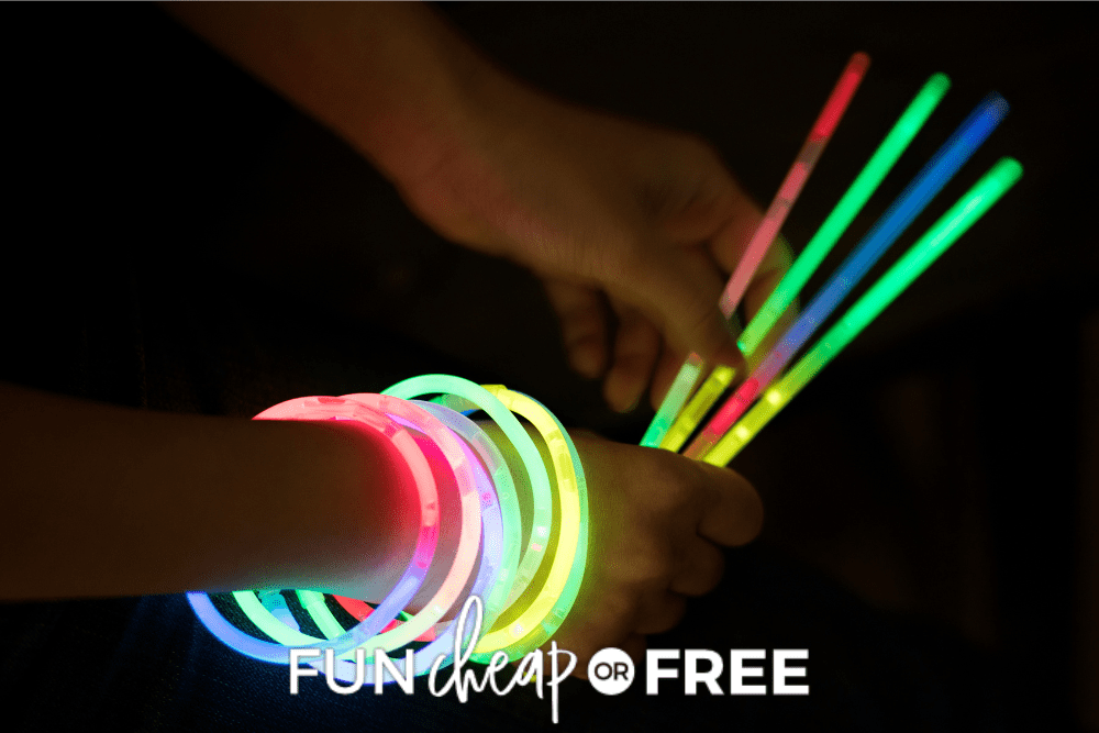 Image of a person's hands with multiple colorful glowing bracelets on on arm, plus more glow sticks in hand. - Fun Cheap Or Free