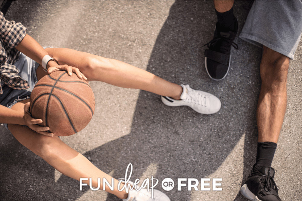 Overhead image of two people sitting on the ground. You can only see their legs. One person is holding a basketball. - Fun Cheap Or Free