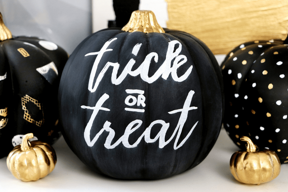 A pumpkin painted with black chalkboard paint with "trick or treat" written in white chalk as a pumpkin decorating idea. 