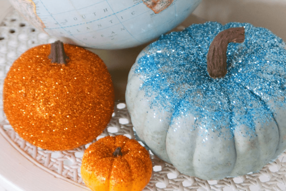 Small pumpkins covered in blue and orange sparkly glitter. 
