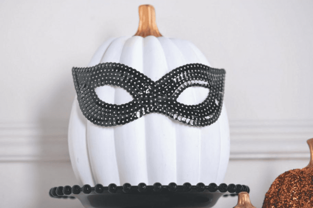 A white pumpkin with a black sequined masquerade mask on. 