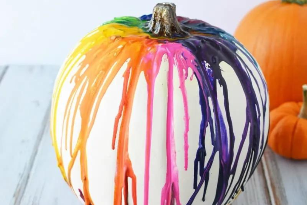 A white pumpkin with colorful melted crayons running down the sides as a no-carve pumpkin decorating idea. 